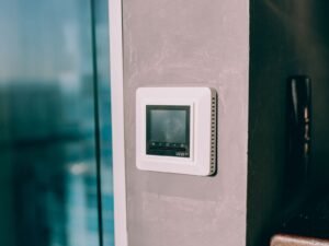 Modern digital thermostat mounted on a wall next to a window, illustrating a wall-mounted smart or programmable thermostat